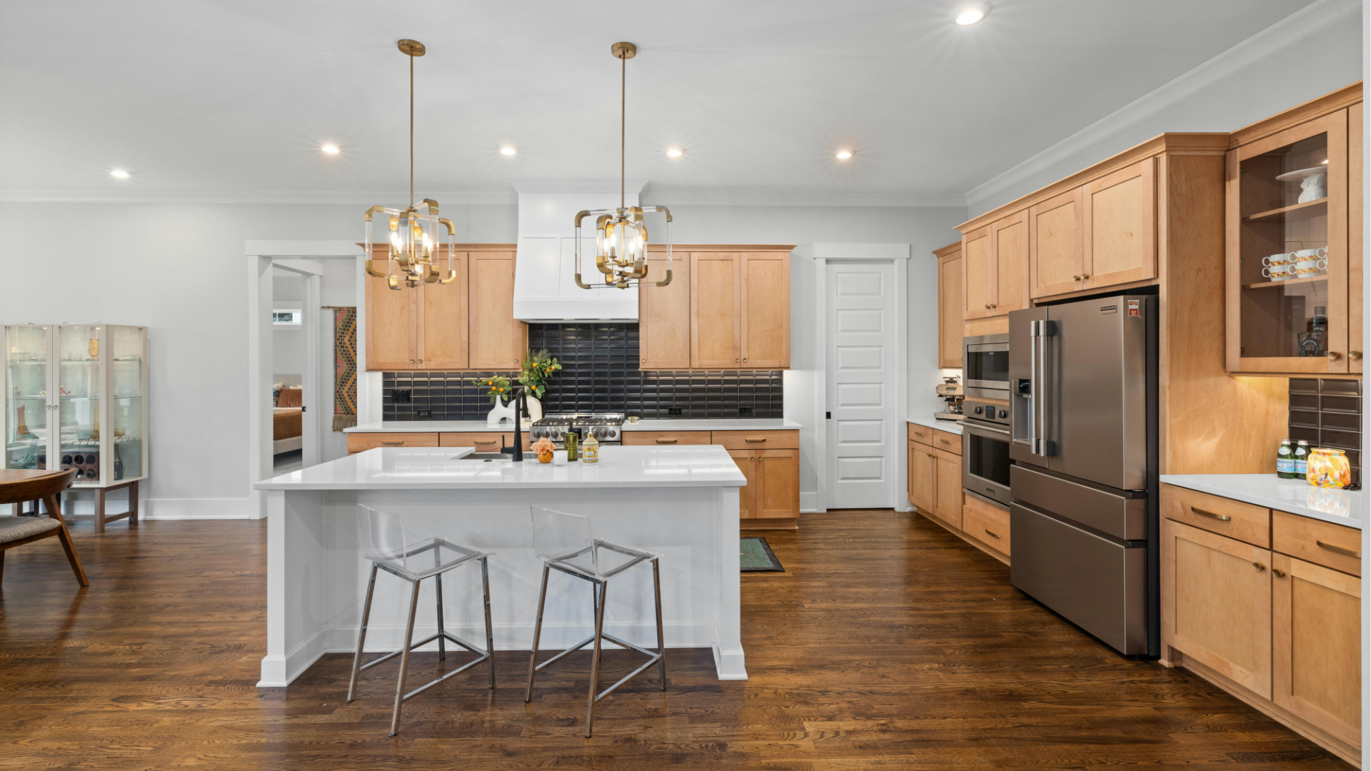 Bright modern kitchen with white island, wood cabinets, stainless appliances, and hanging pendant lights