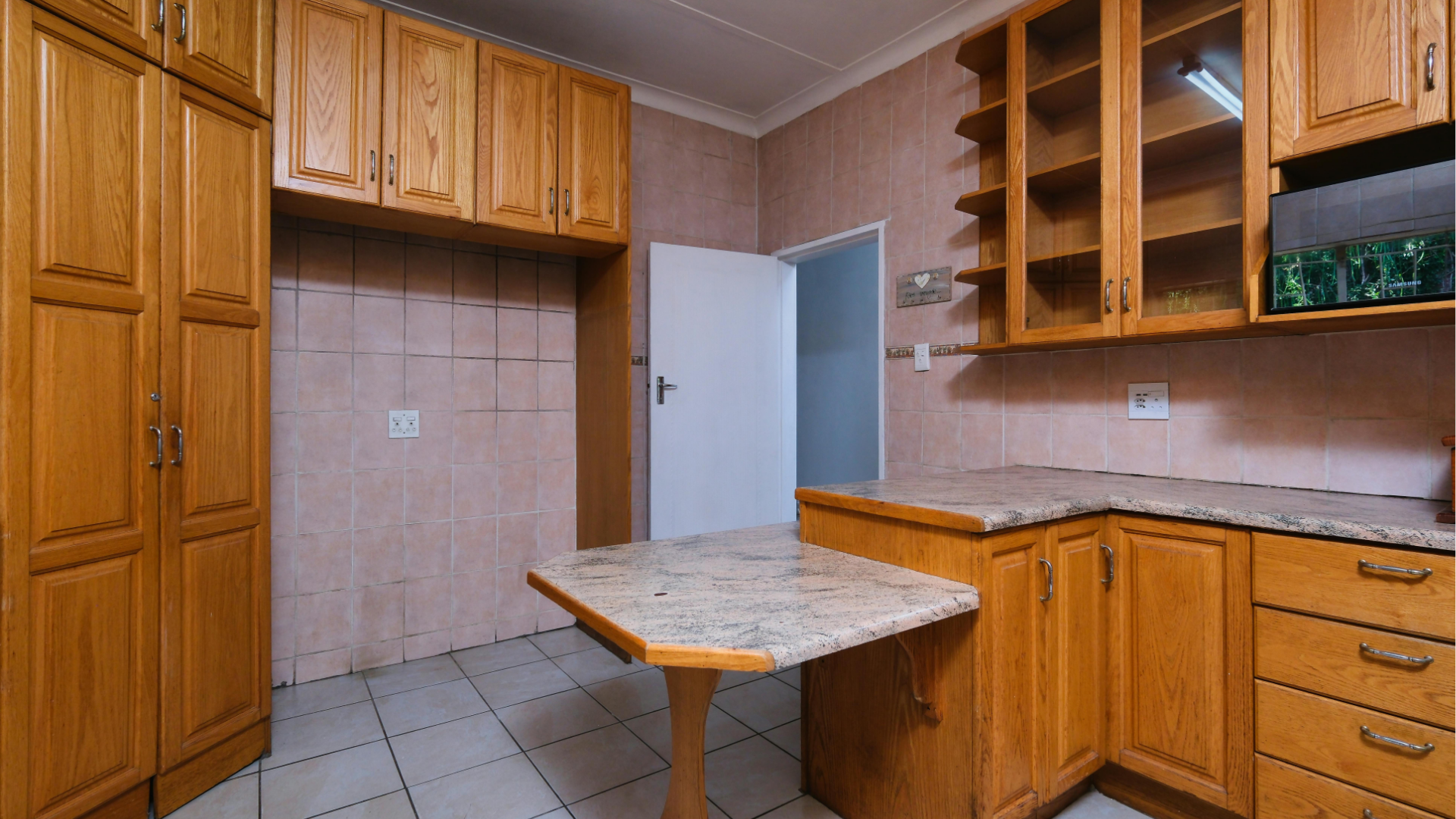 Empty kitchen with wooden cabinets, tiled floor, and a small marble-topped table near an open door.