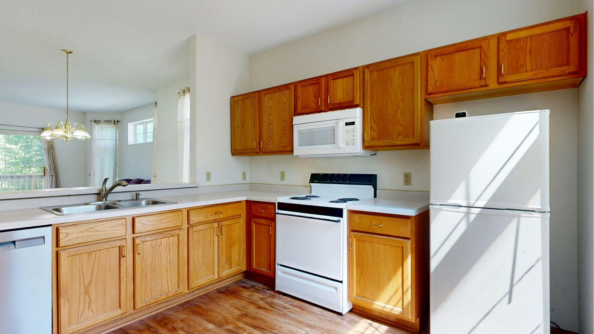 Bright kitchen with wooden cabinets, white appliances, and a breakfast bar in a sunlit home interior