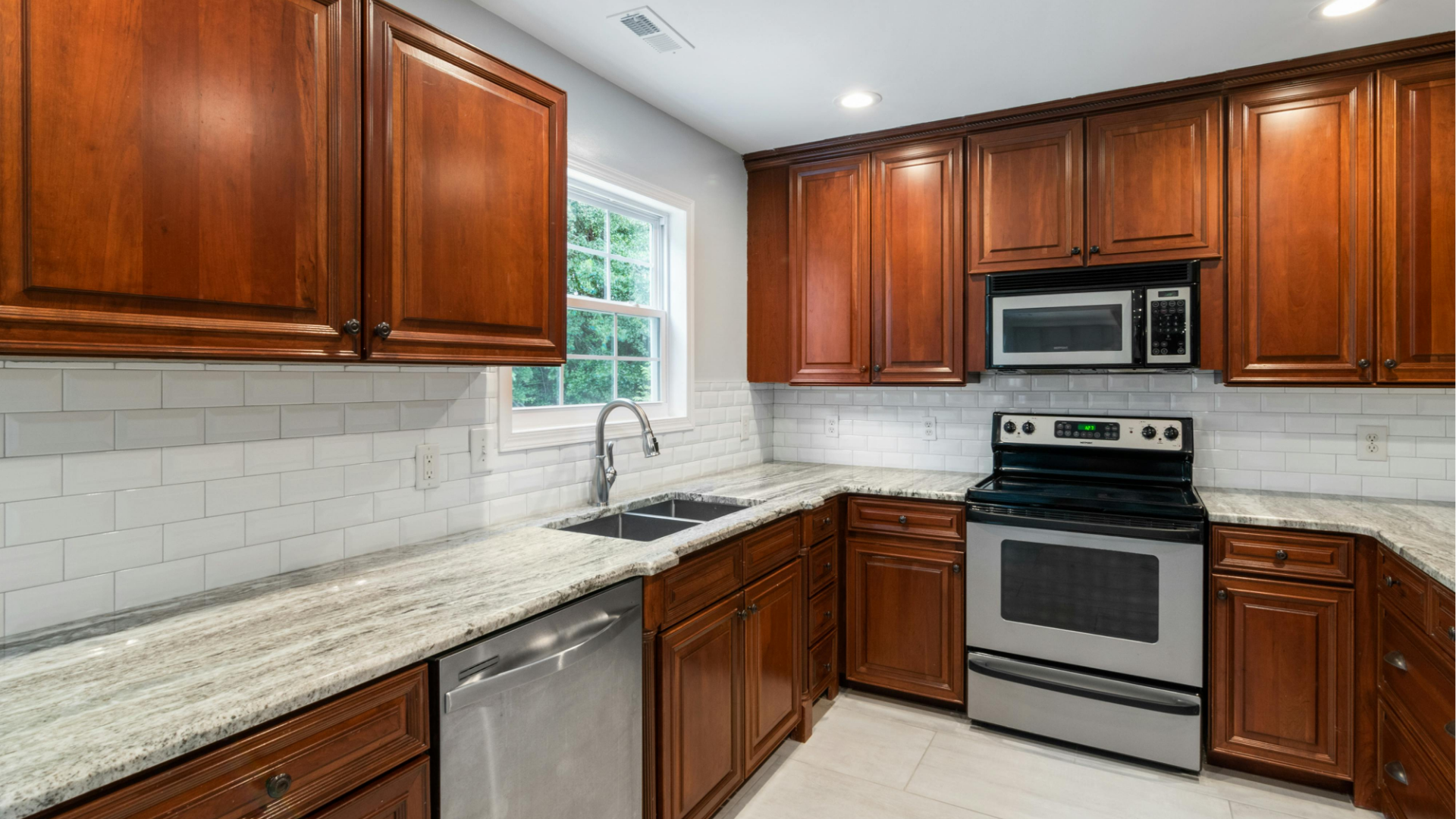 Modern kitchen with cherry wood cabinets, white countertops, gray backsplash, and stainless steel appliances.