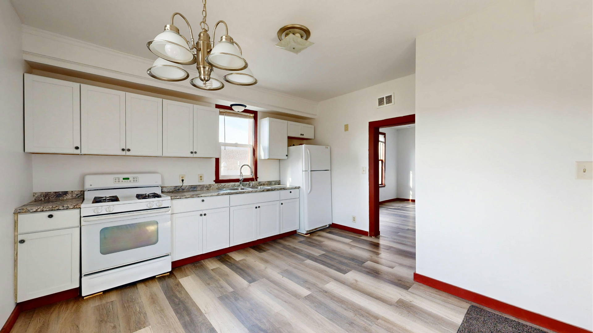 Empty kitchen with white cabinets, stove, refrigerator, and wood-look flooring in a bright room