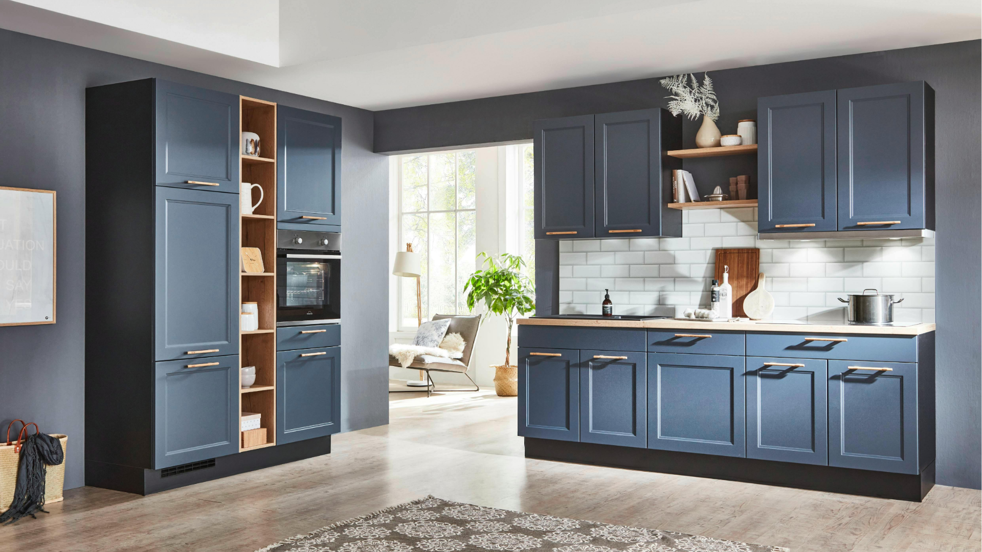 Modern blue kitchen with island, tall pantry cabinet, and windowed breakfast nook in the background