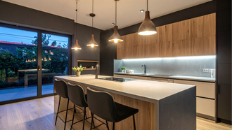 Modern kitchen with large island, pendant lights, wood cabinets, and sliding glass doors to a patio.