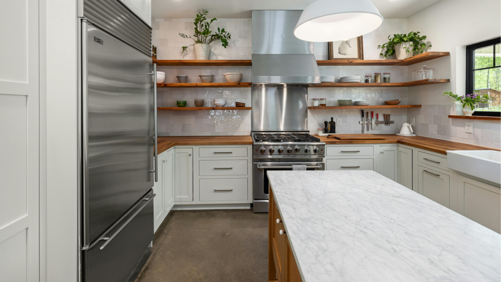 Bright modern kitchen with stainless steel appliances, white cabinets, wood shelves, and a marble island.