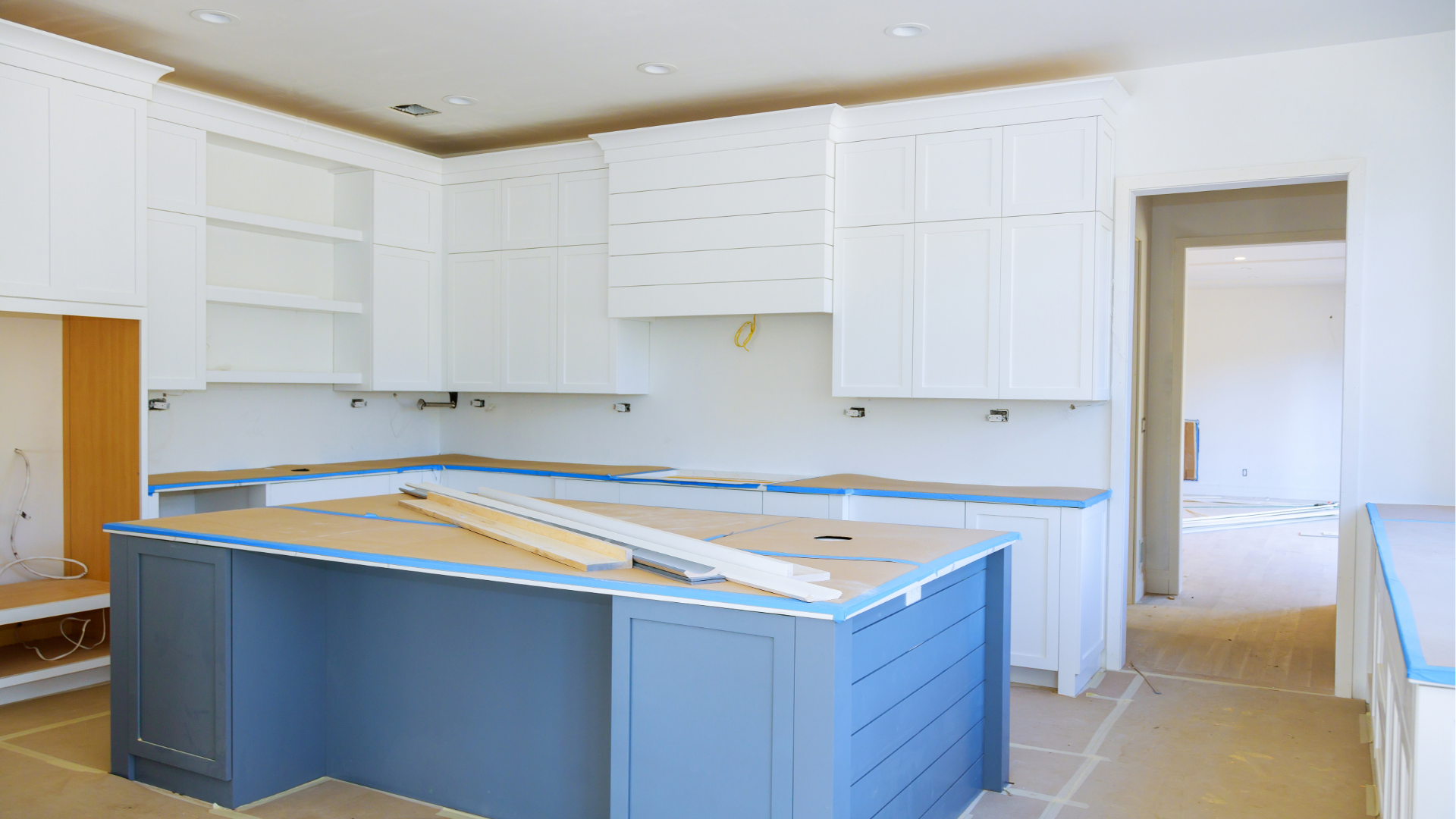 Bright unfinished kitchen with white cabinets and a blue island under construction