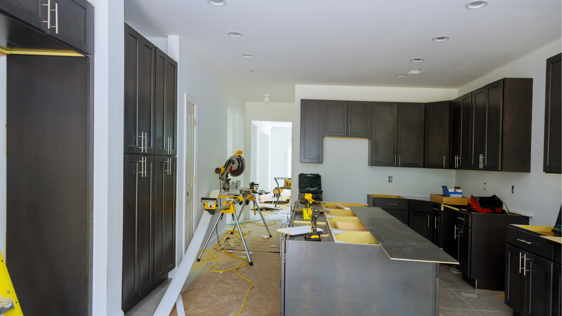 Modern kitchen under renovation with dark cabinets, tools, and a ladder on the floor