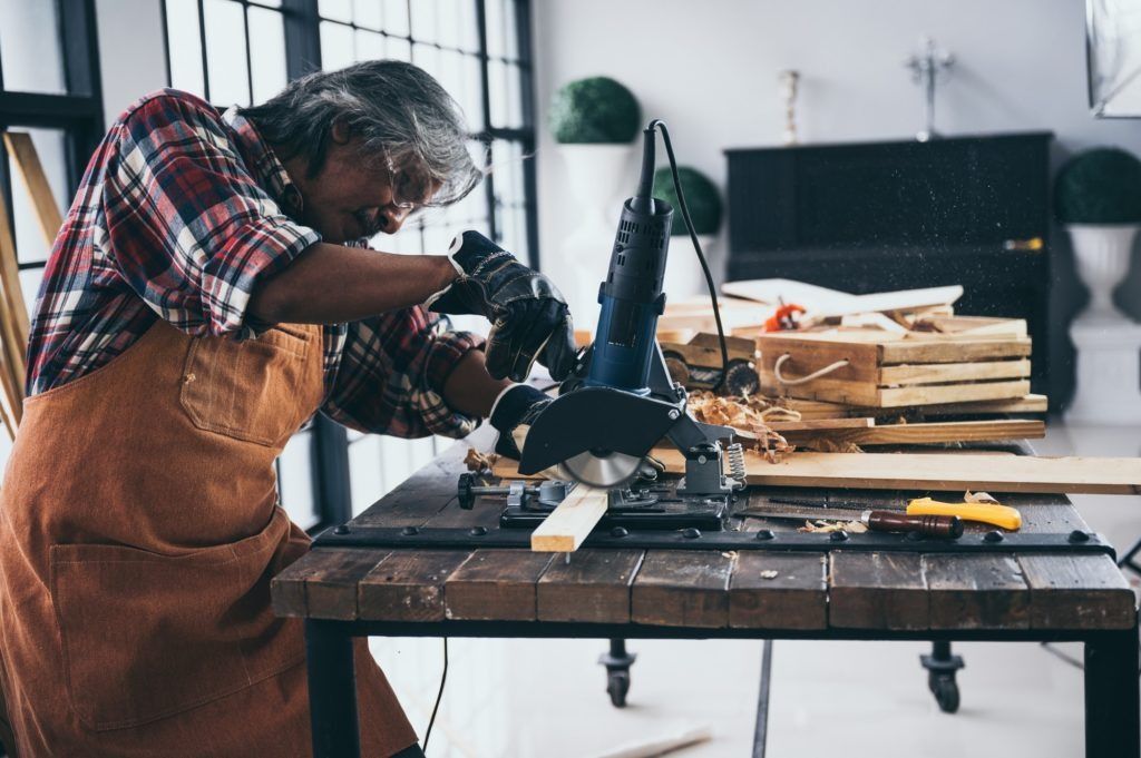 Woodworker in a workshop sanding a wooden table with power tools and scattered tools nearby