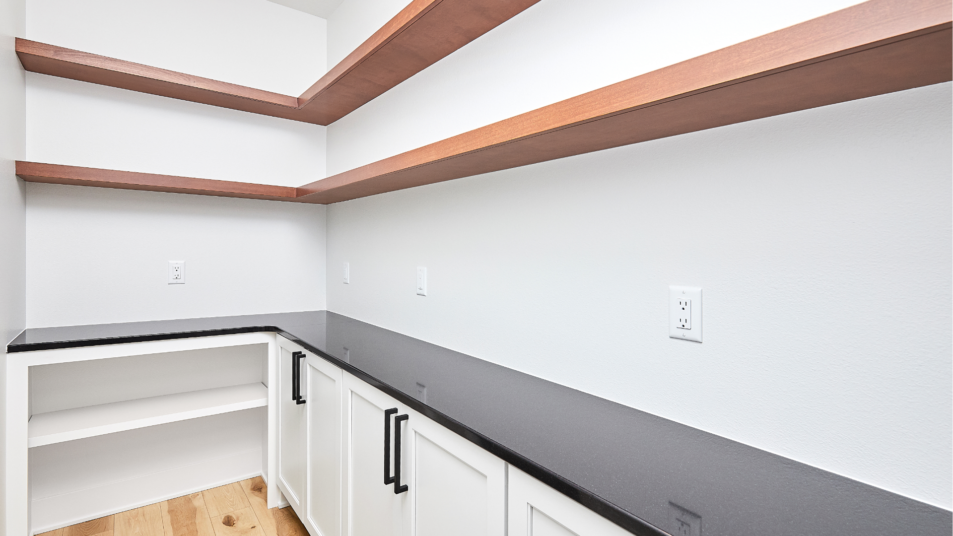 Empty white laundry room with dark countertops, white cabinets, and wood-trimmed shelves.