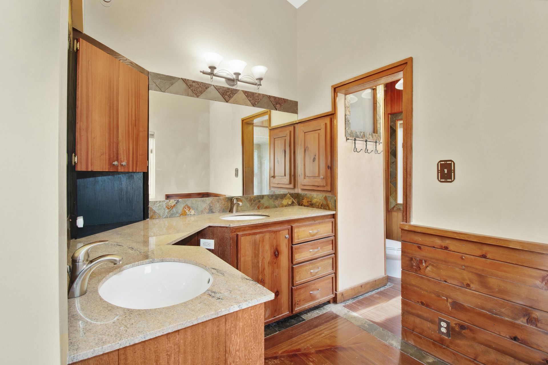 Bathroom vanity with wood cabinets, beige countertop, and sink in a small tiled room.
