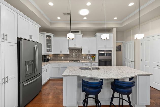 Modern white kitchen with marble island, stainless steel appliances, and blue barstools