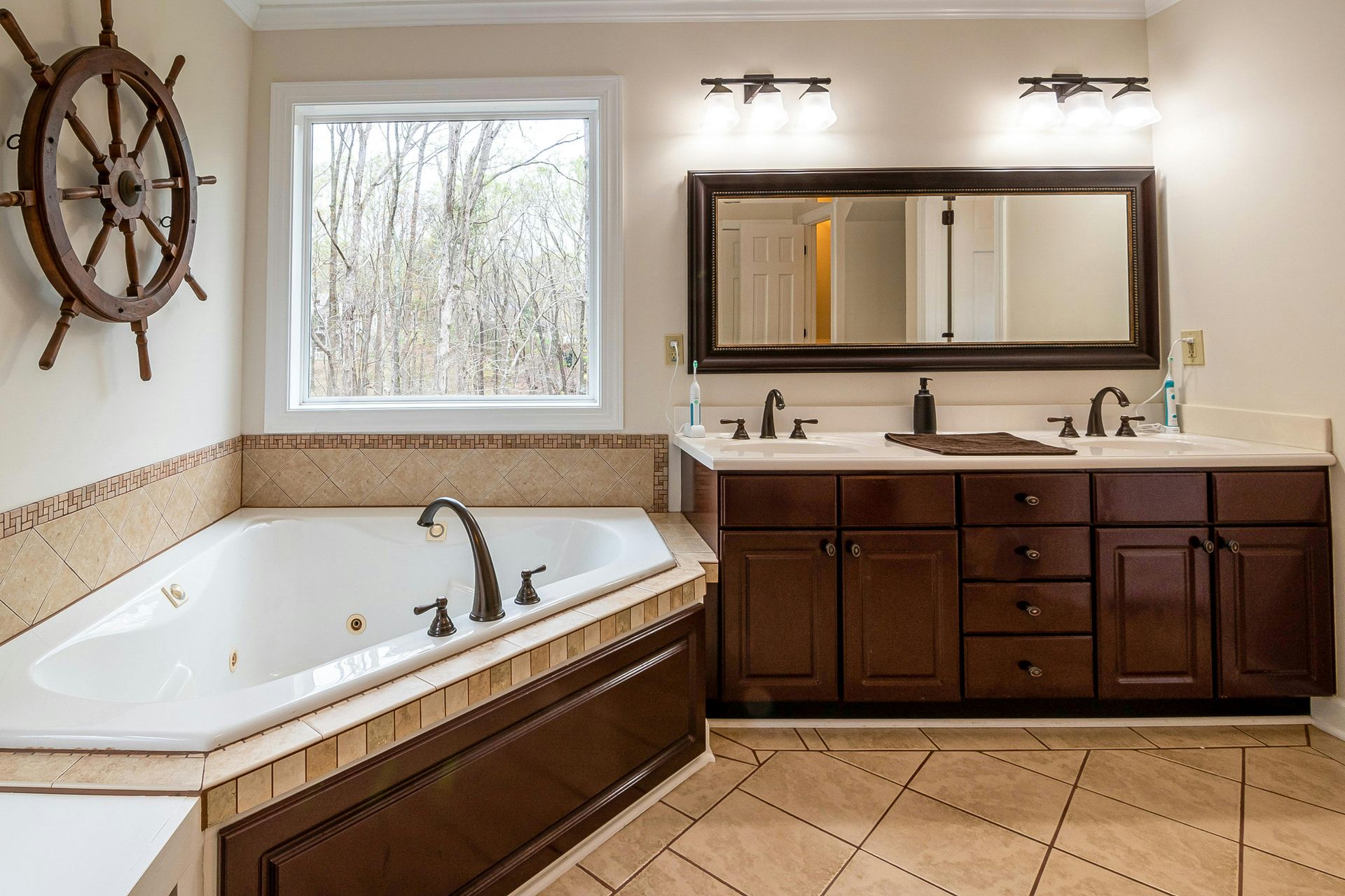 Luxurious bathroom with corner jetted tub, dark wood vanity, large mirror, and nautical wall decor