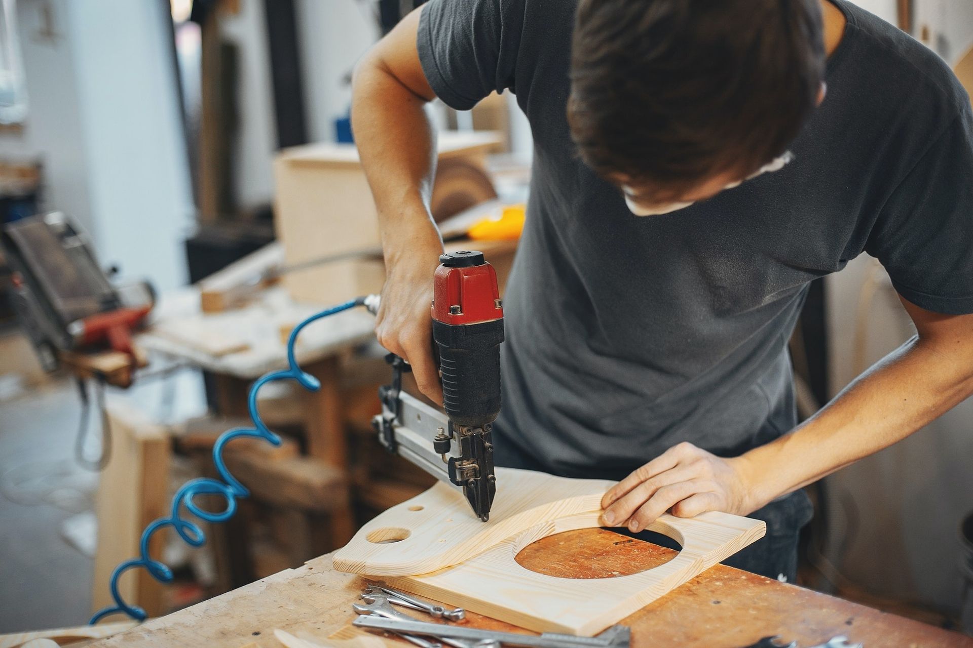 Person using a drill to cut a circular hole in wood at a workshop bench