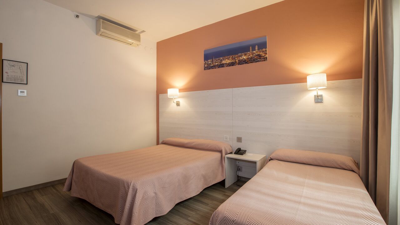 Hotel room with two beds, peach and white walls, small nightstand, city photo.