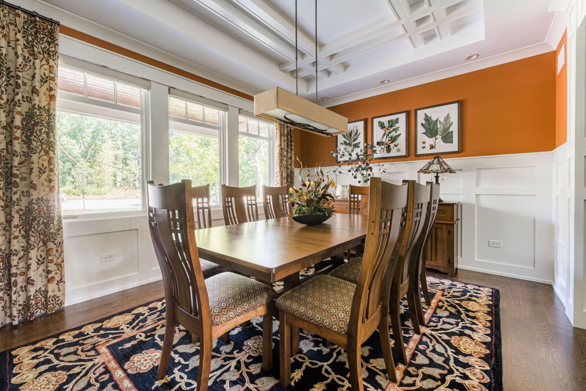 A dining room with a long wooden table and chairs and a rug.
