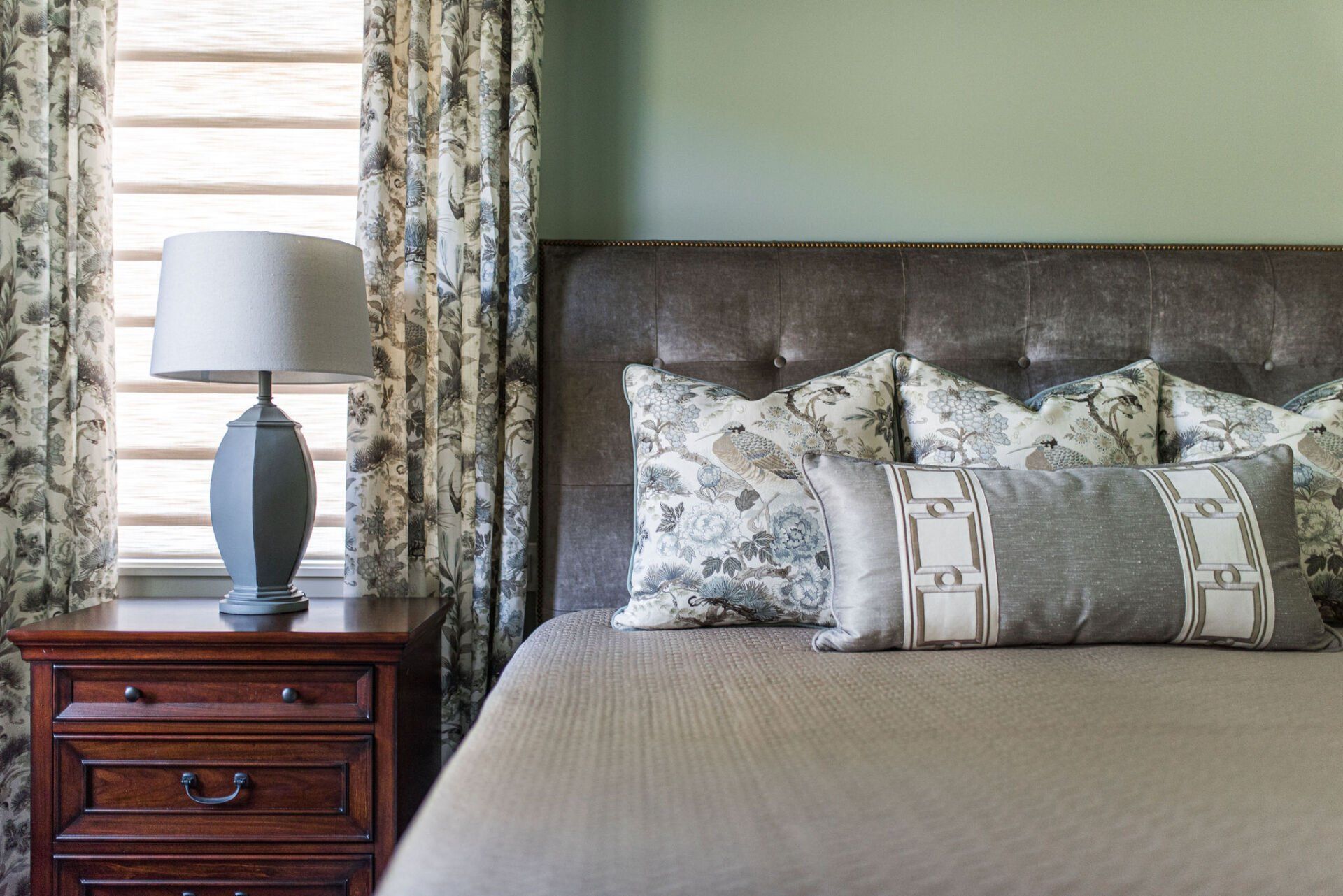 A bedroom with a bed , nightstand , lamp and window.