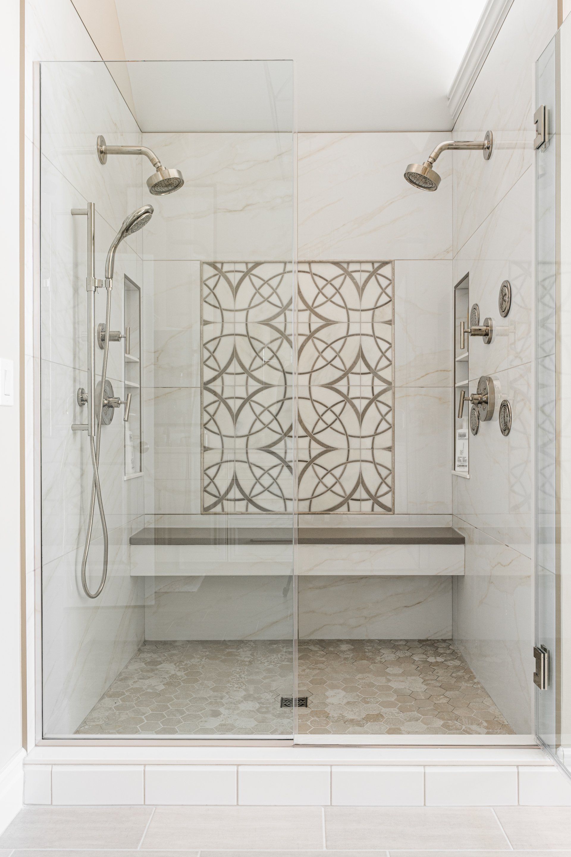 A walk in shower with two shower heads and a bench.
