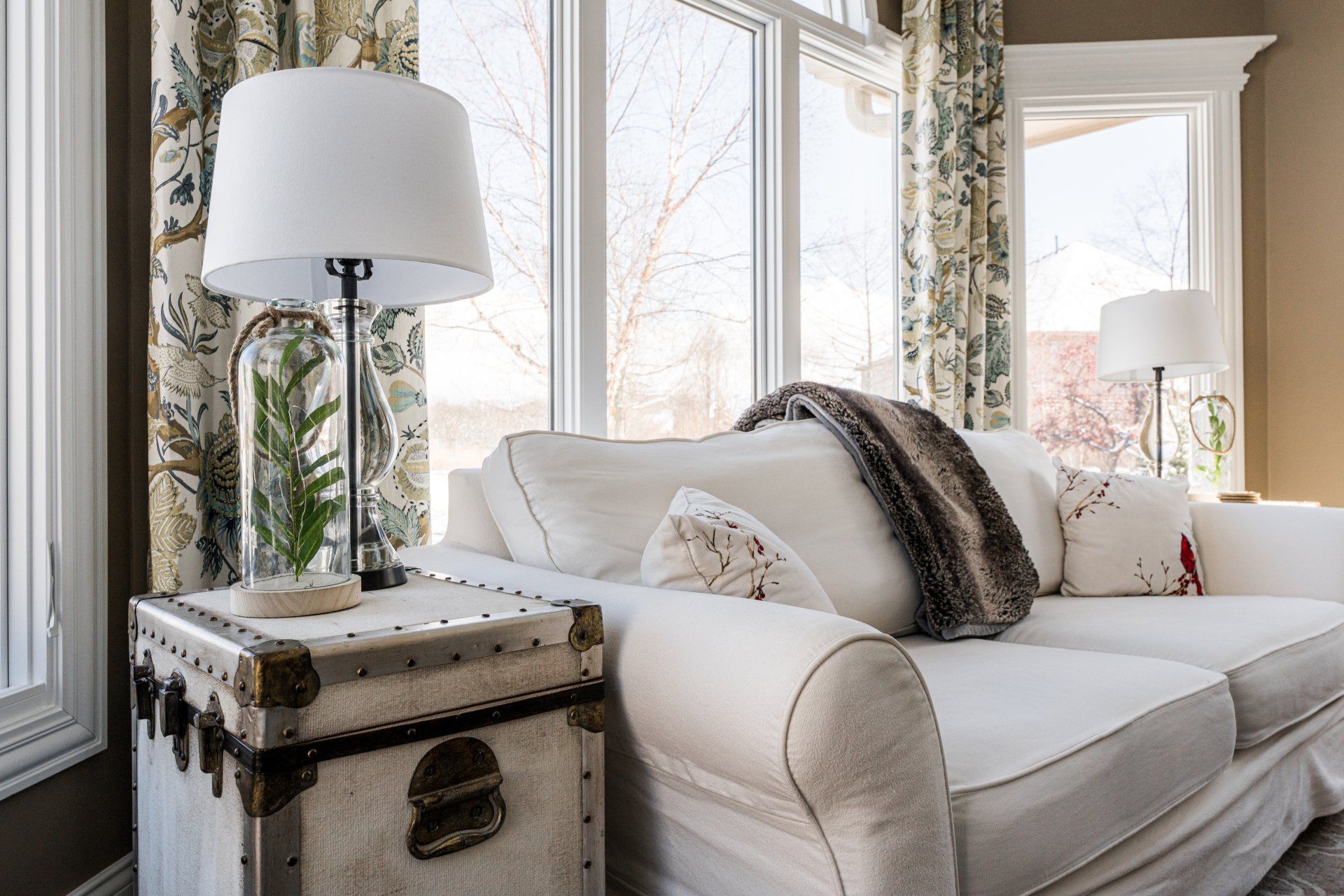 A living room with a white couch , lamp , and trunk.
