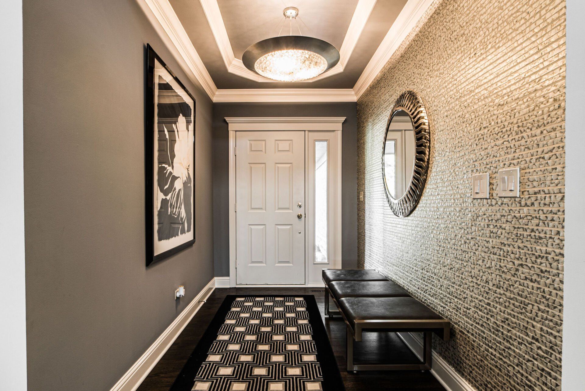 A hallway with a bench , mirrors , and a rug.