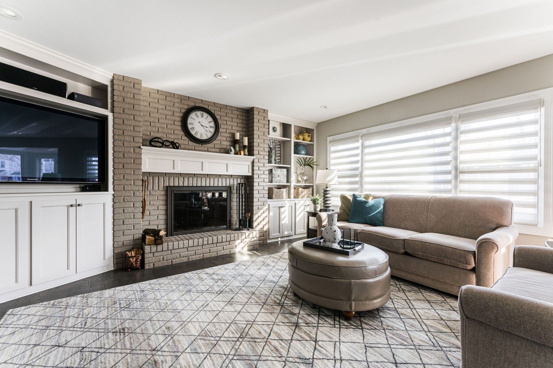 A living room with a couch , chairs , ottoman , fireplace and television.