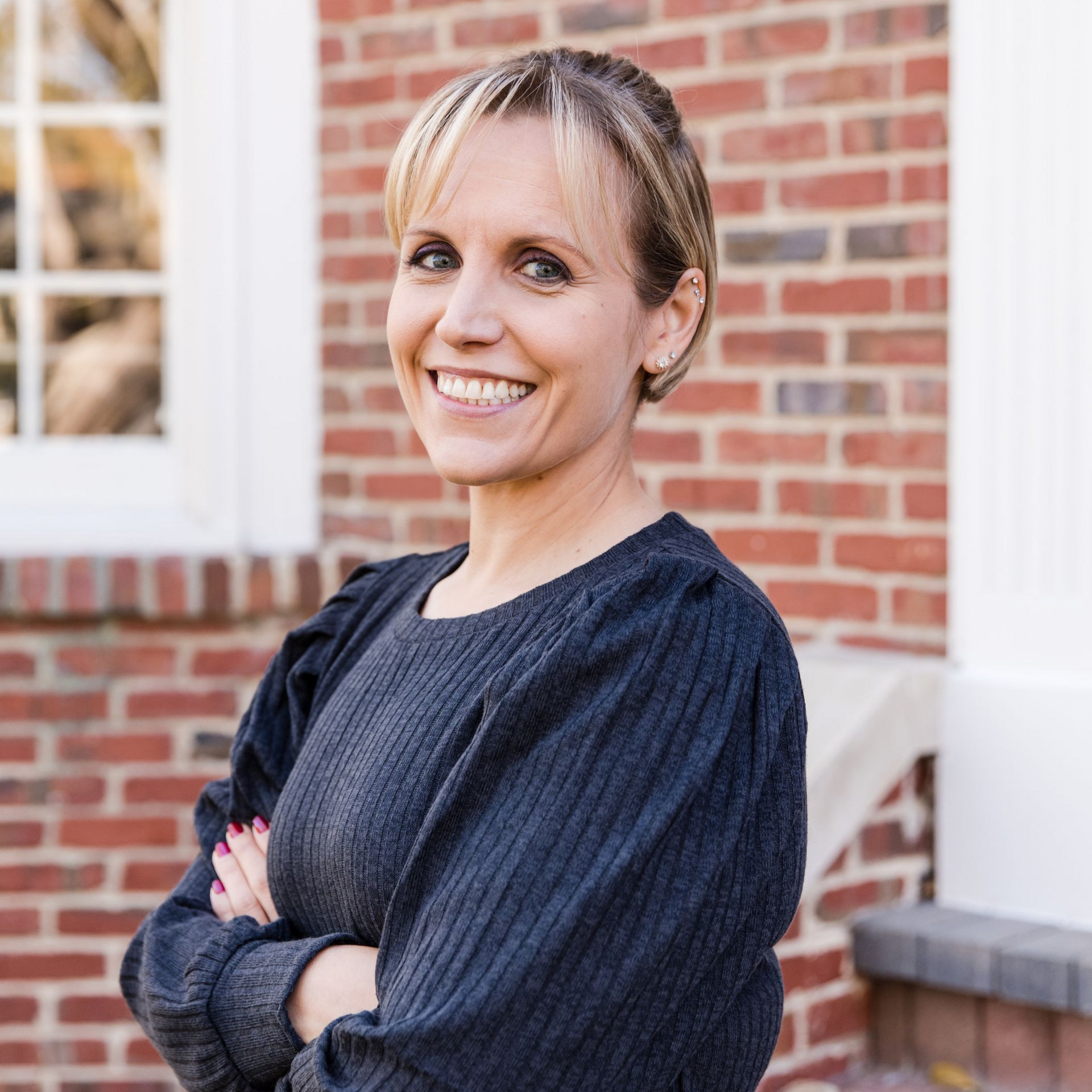 A woman in a blue shirt and black jacket is smiling for the camera.