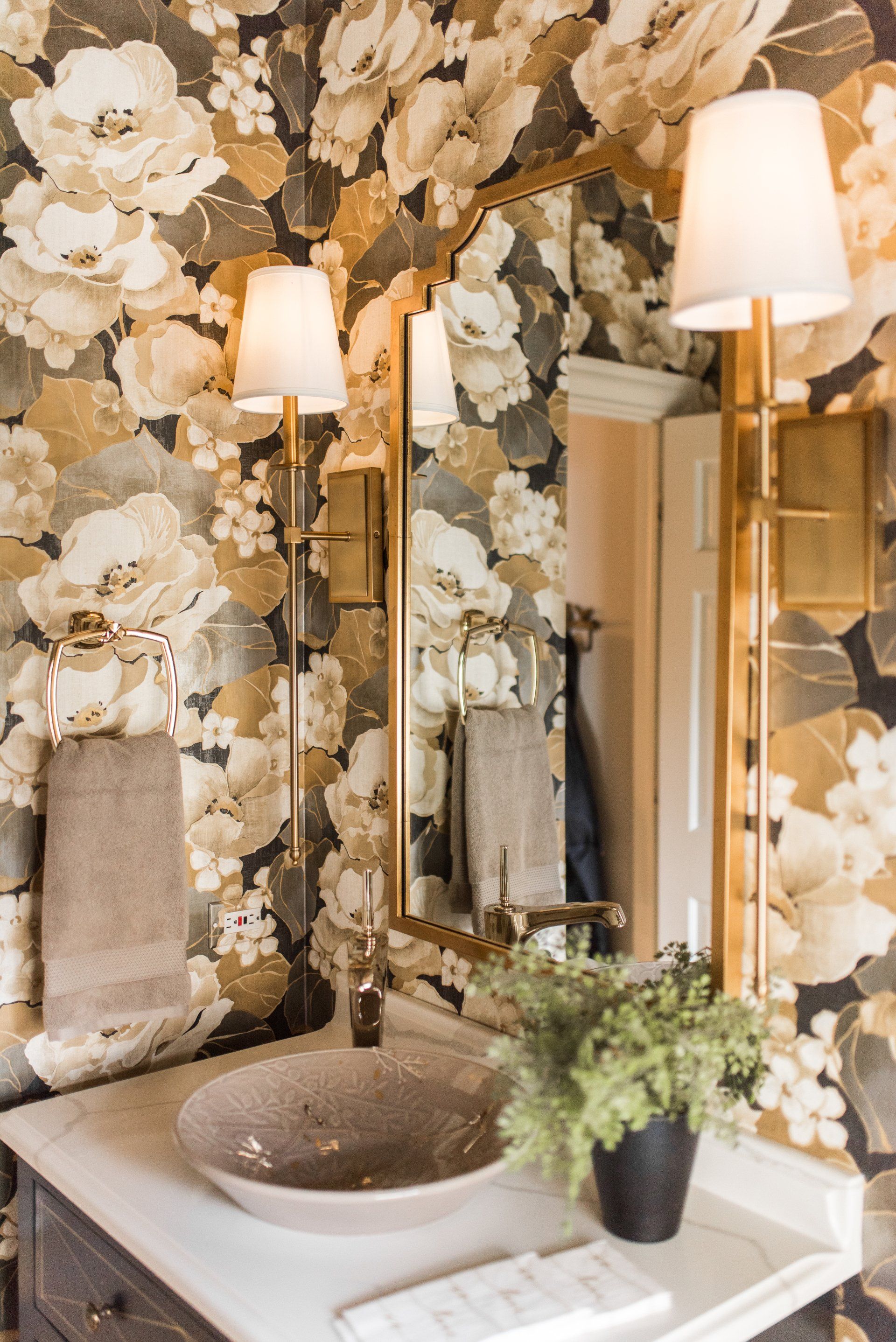 A bathroom with a sink , mirror , and floral wallpaper.