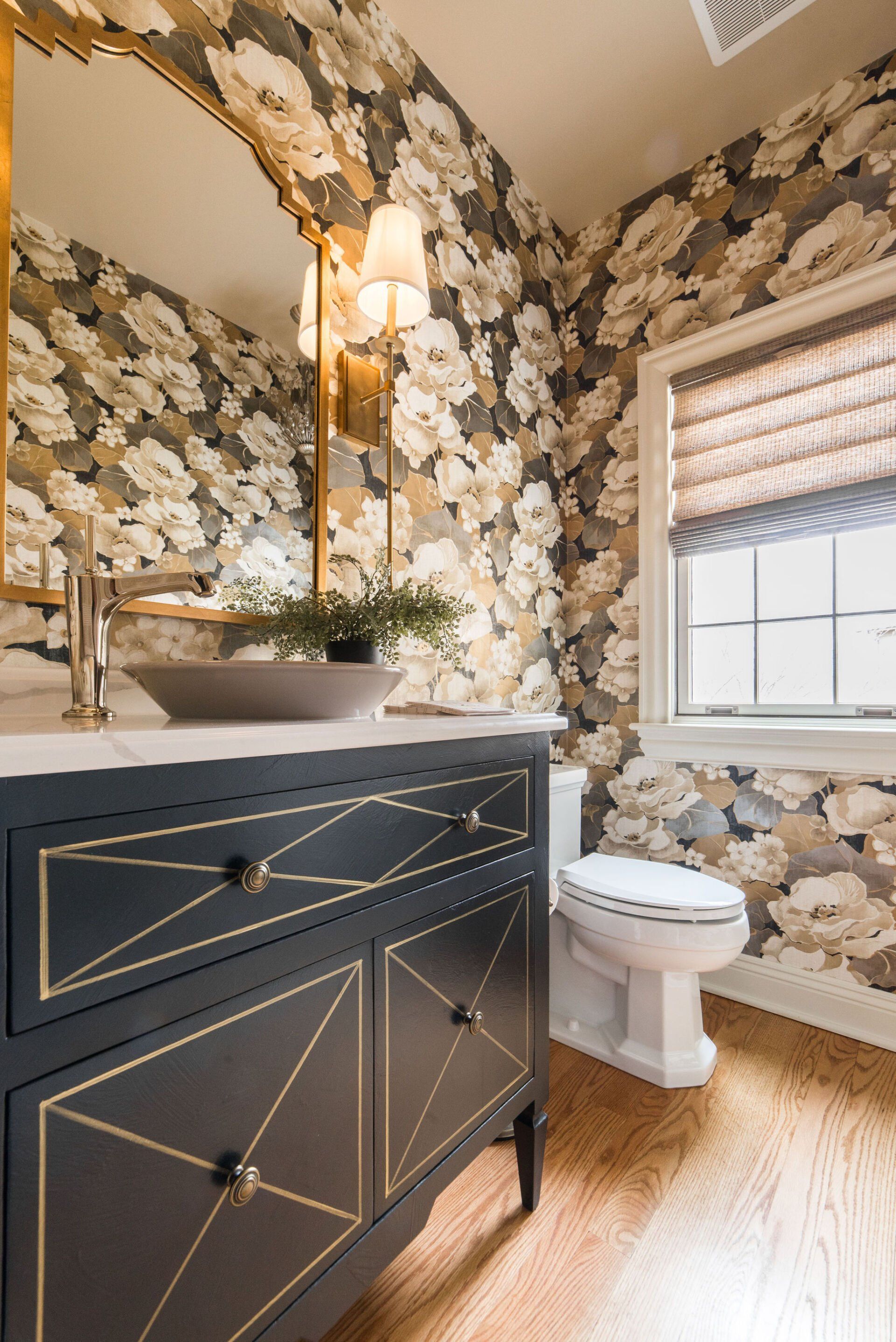 A bathroom with a sink , toilet , mirror and floral wallpaper.