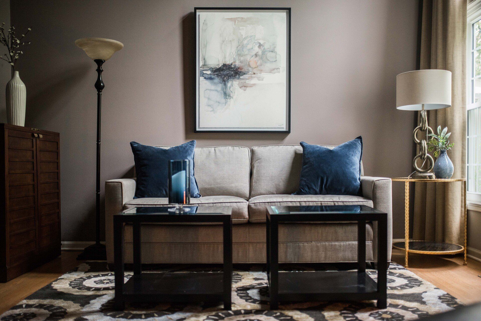 A living room with a couch , coffee table , lamp and painting on the wall.