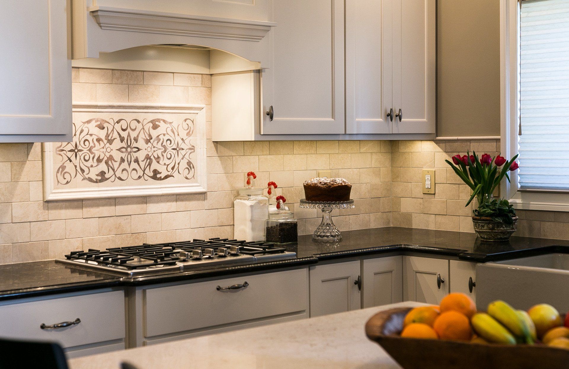 A kitchen with a stove top oven and a bowl of fruit on the counter.