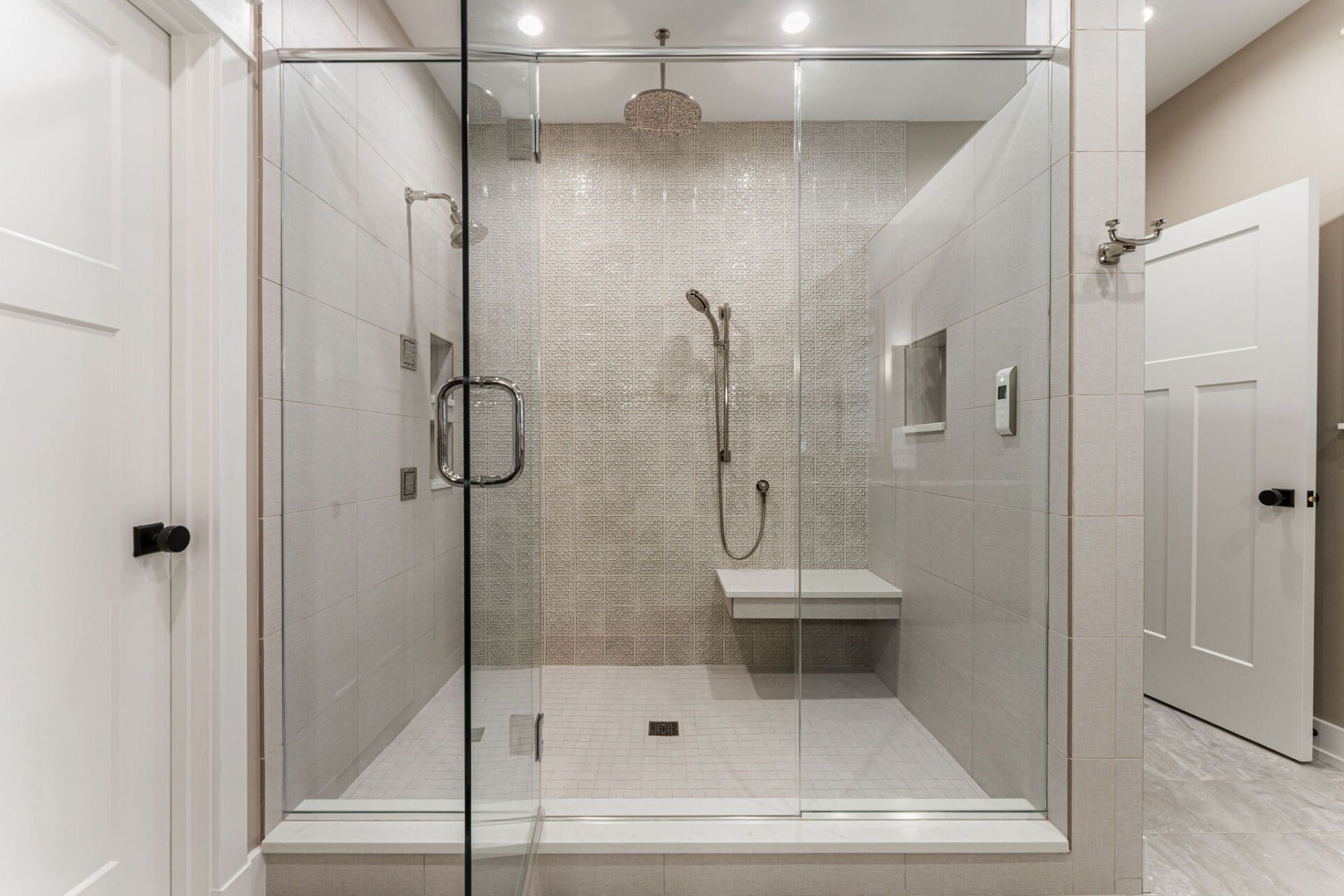 A bathroom with a walk in shower with a glass door and a bench.