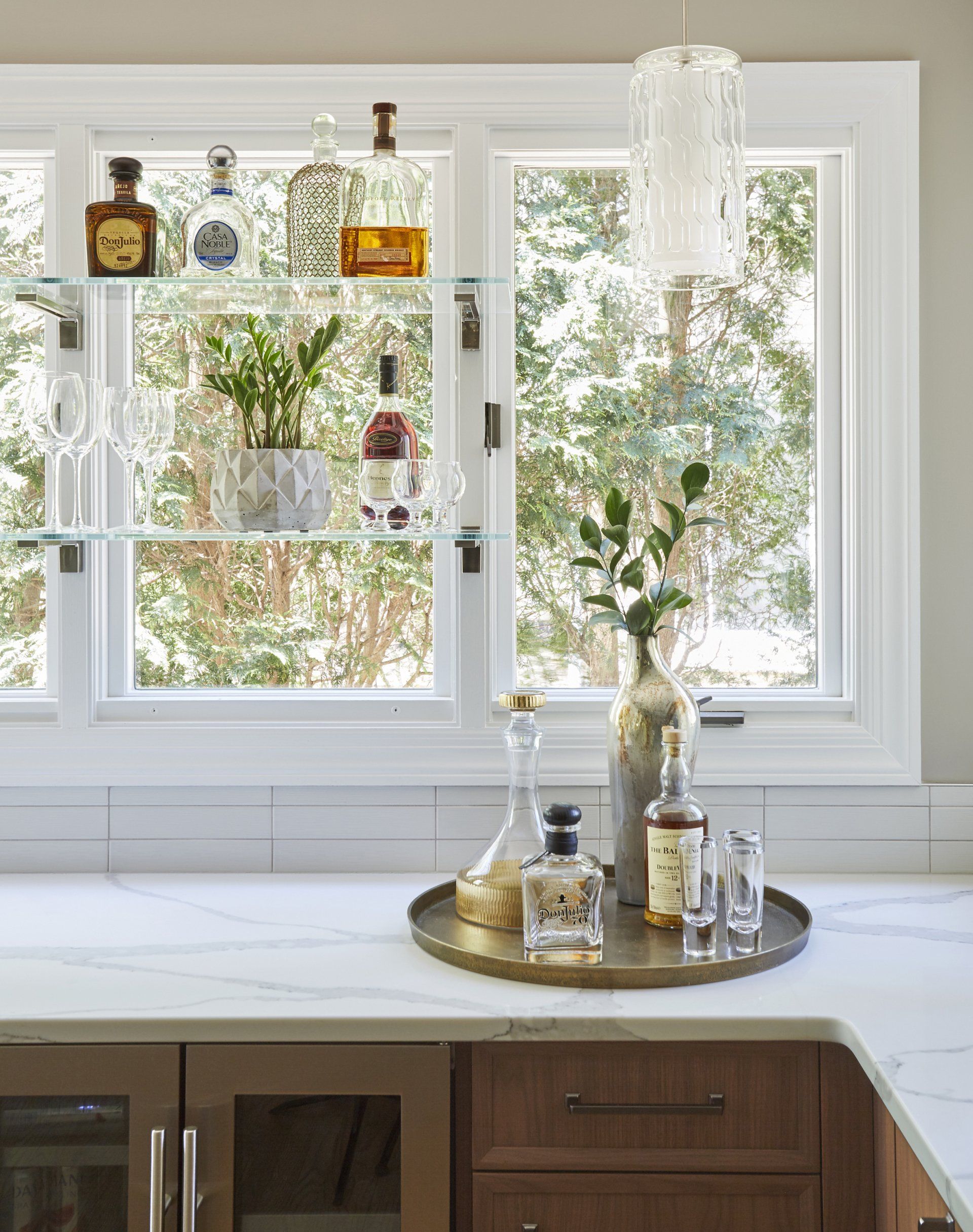 A kitchen counter with bottles and glasses on it and a window.