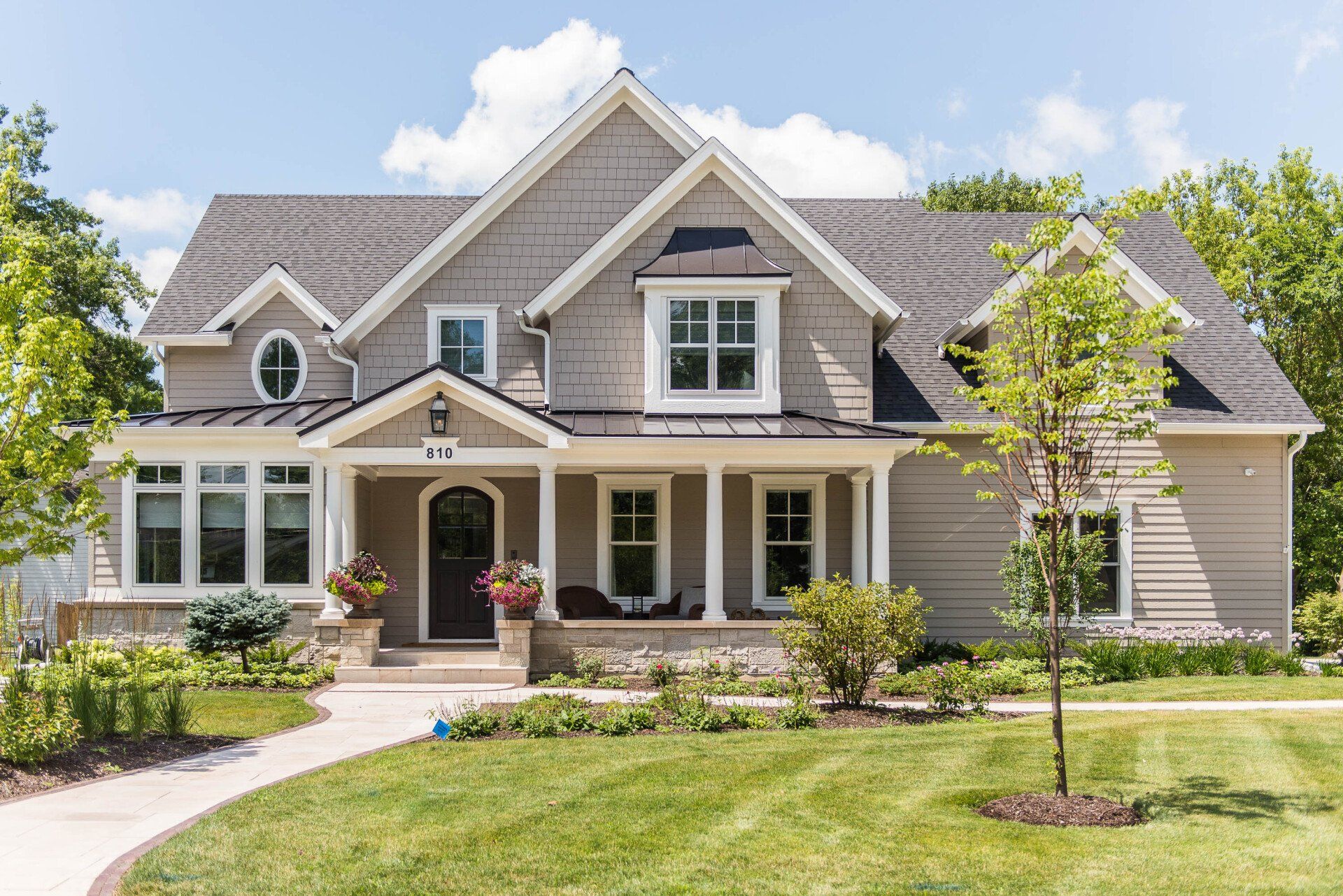 A large house with a large porch and a lot of windows is sitting on top of a lush green lawn.