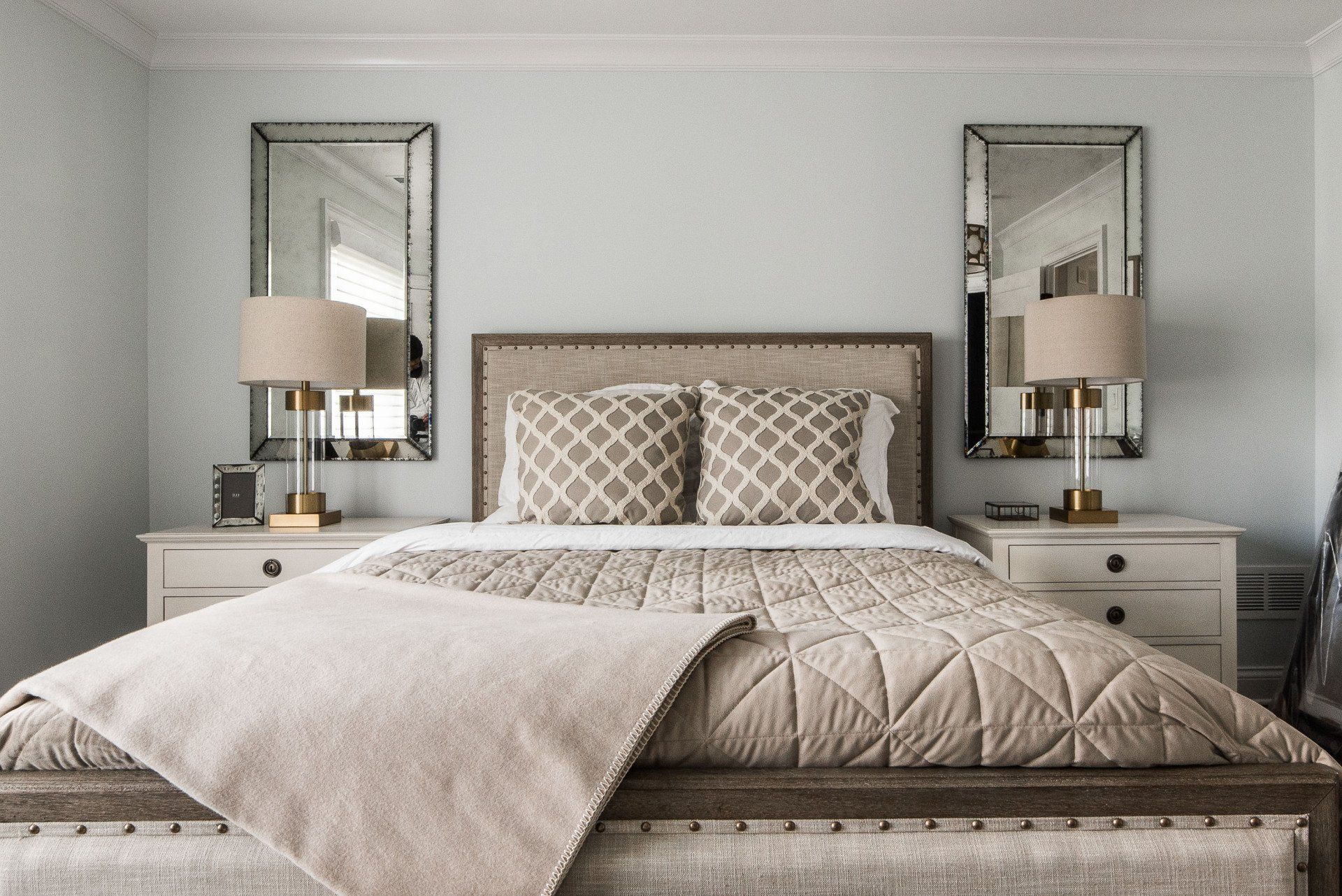 A bedroom with a bed , two nightstands , two mirrors and two lamps.