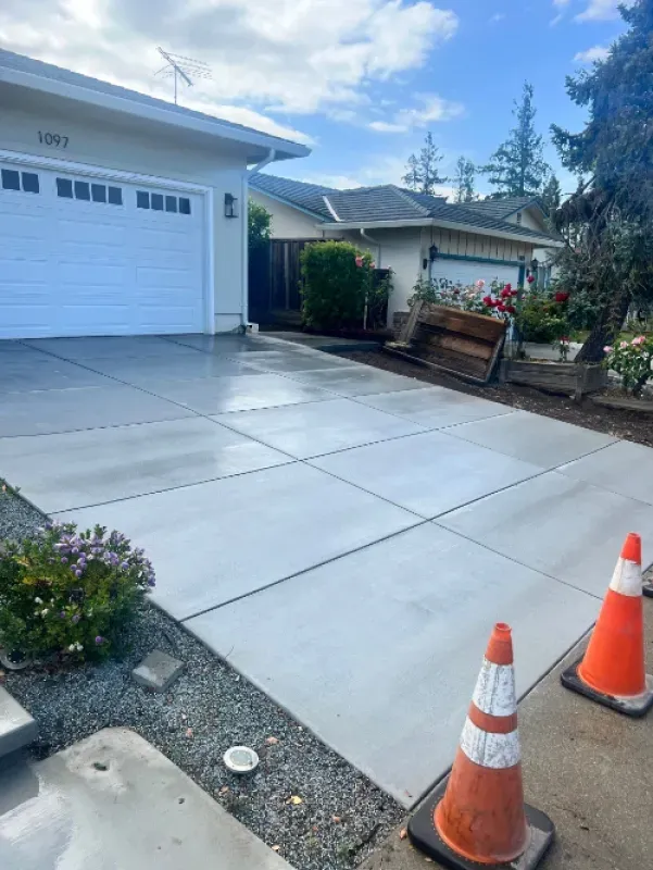 Driveway with fresh concrete slabs, orange traffic cones, and a garage in front of a house.