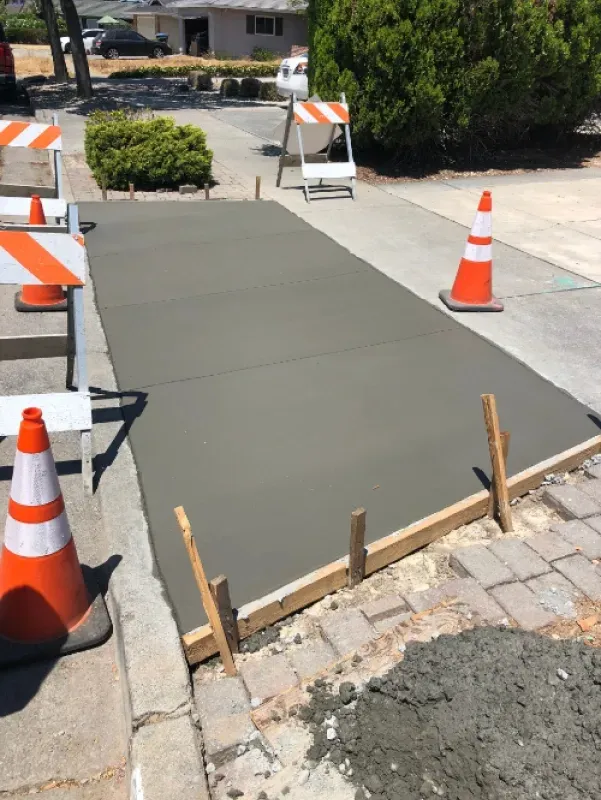 Fresh concrete sidewalk repair with orange cones and barricades on a residential street