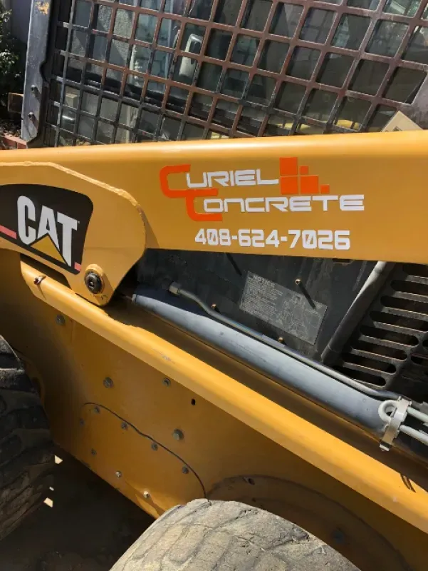 CAT skid steer with Curiel Concrete logo and phone number on yellow arm