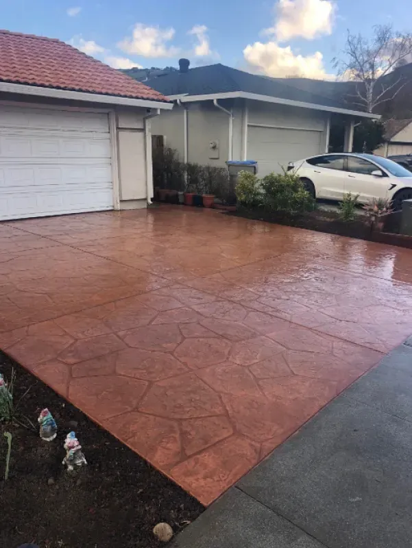 Driveway with red stamped concrete, garage, parked white car, and potted plants beside a house.