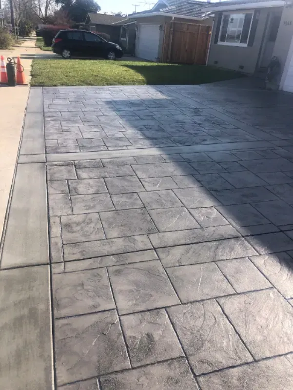 Concrete driveway beside a small lawn and house, with a parked black SUV in the background.