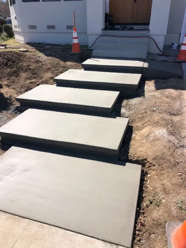 Concrete stepping stones leading to a front porch entrance, with an orange traffic cone nearby.