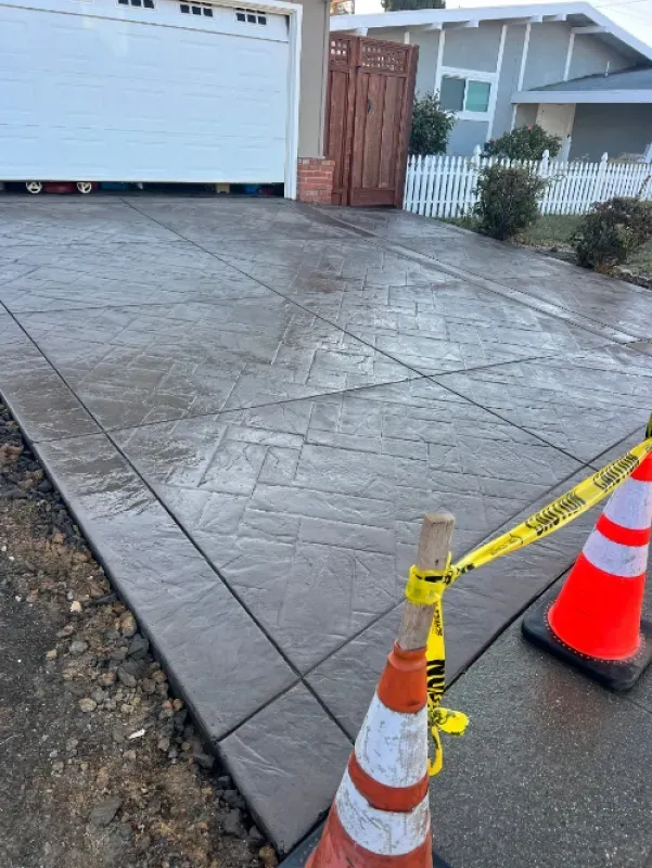Freshly stamped concrete driveway with traffic cones and caution tape near a garage and sidewalk