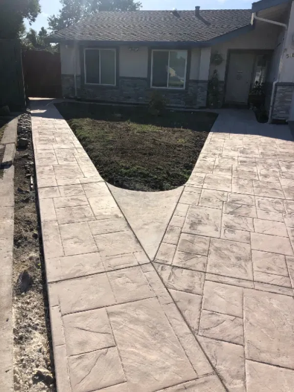 Stamped concrete walkway leading to a house front door around a triangular mulch bed.