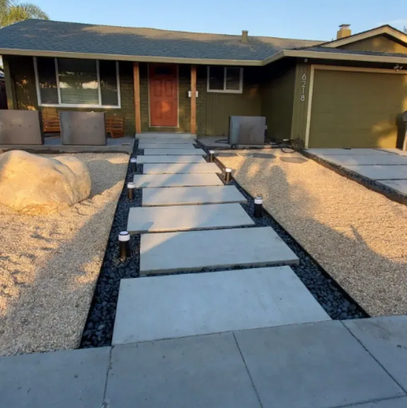 Front yard walkway with stepping stones leading to a house entrance, flanked by gravel landscaping.