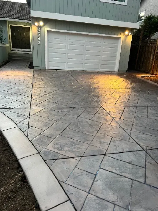 Stamped concrete driveway leading to a lit garage door at dusk