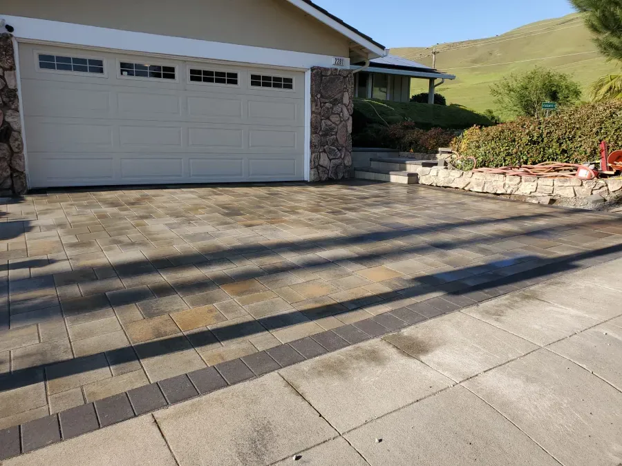 Driveway with garage, stone paving, and hillside landscaping in daylight