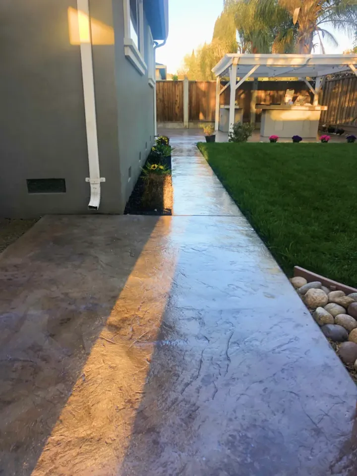 Stamped concrete walkway beside a house leading to a backyard patio and lawn at sunset