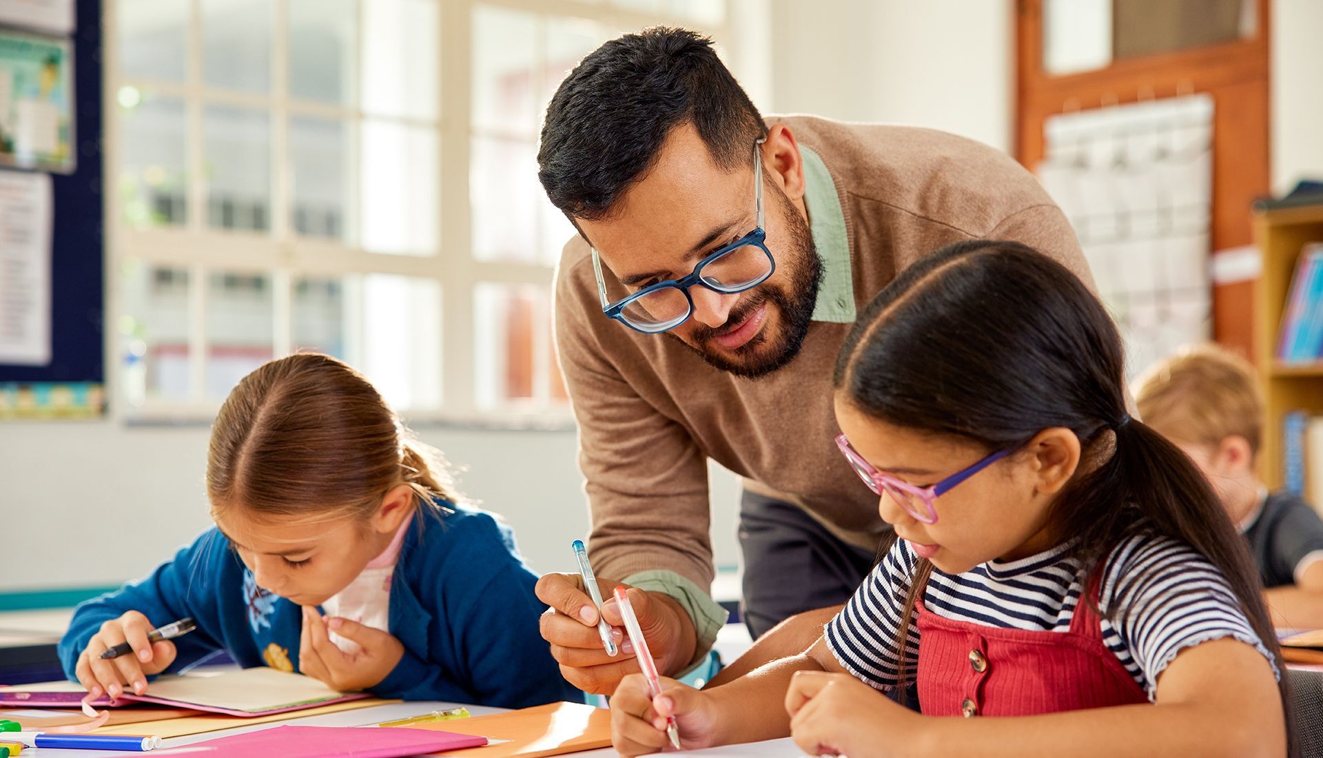 Teacher helping two children with arts and crafts at a classroom table