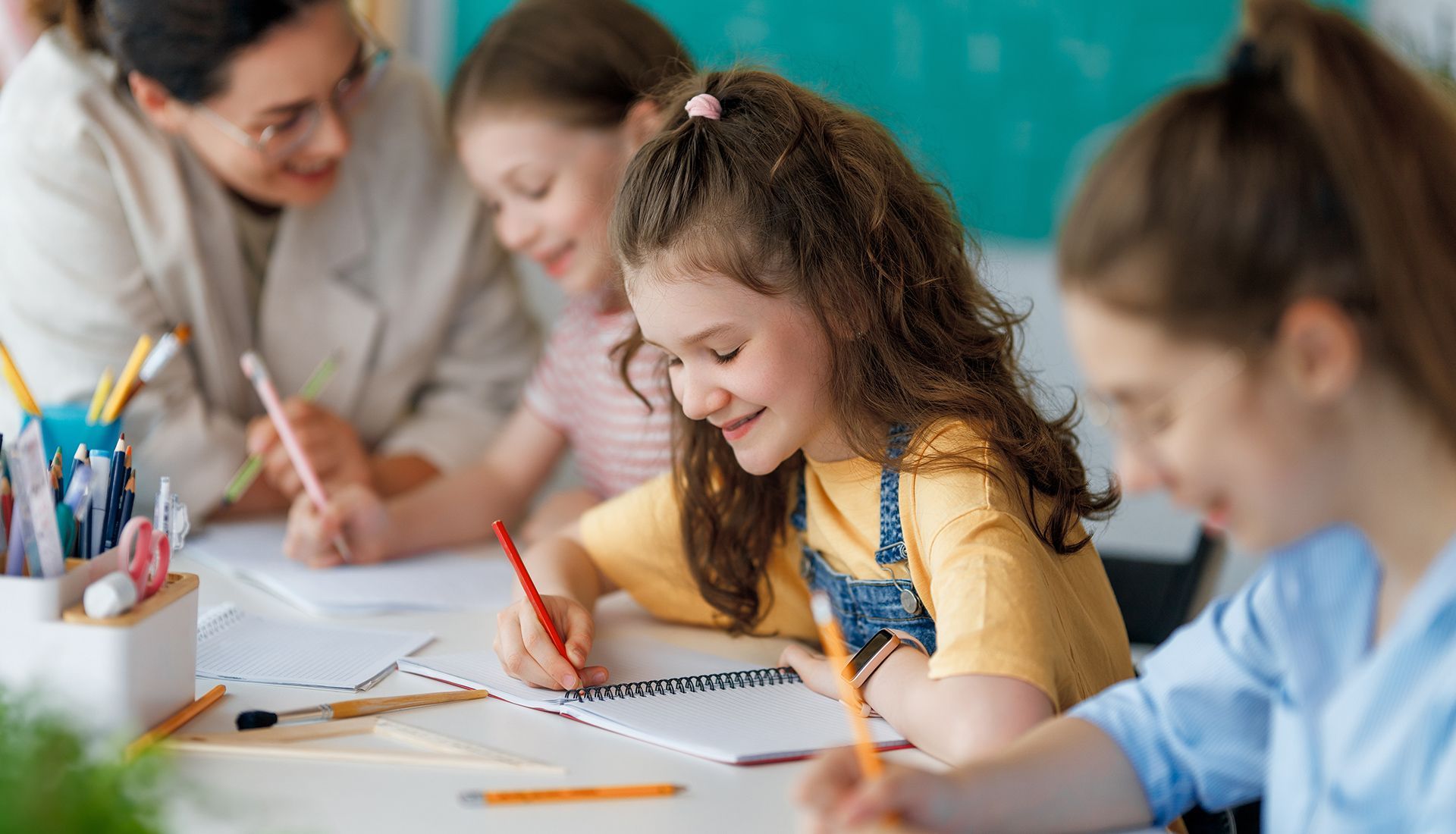 Teacher assisting students writing at desk in classroom.