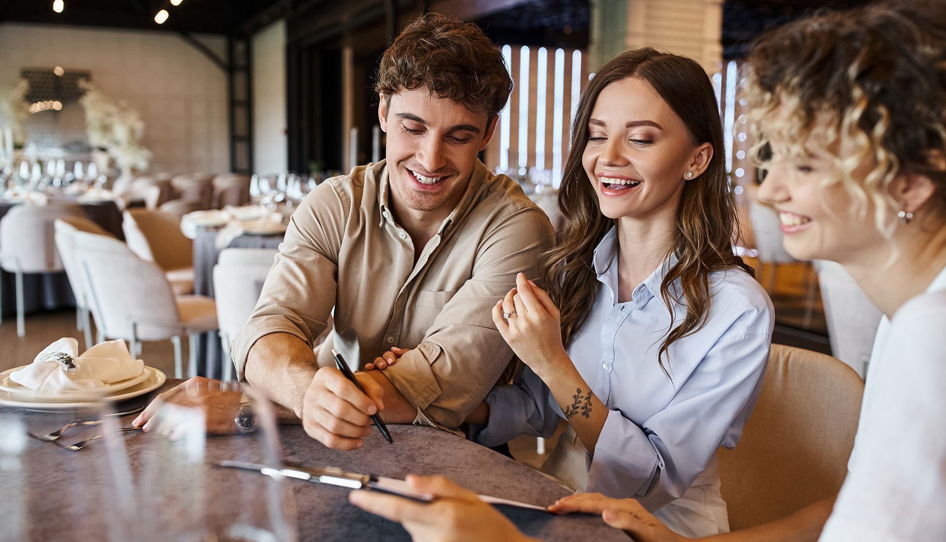 Three friends laughing over drinks at a café table while looking at a smartphone
