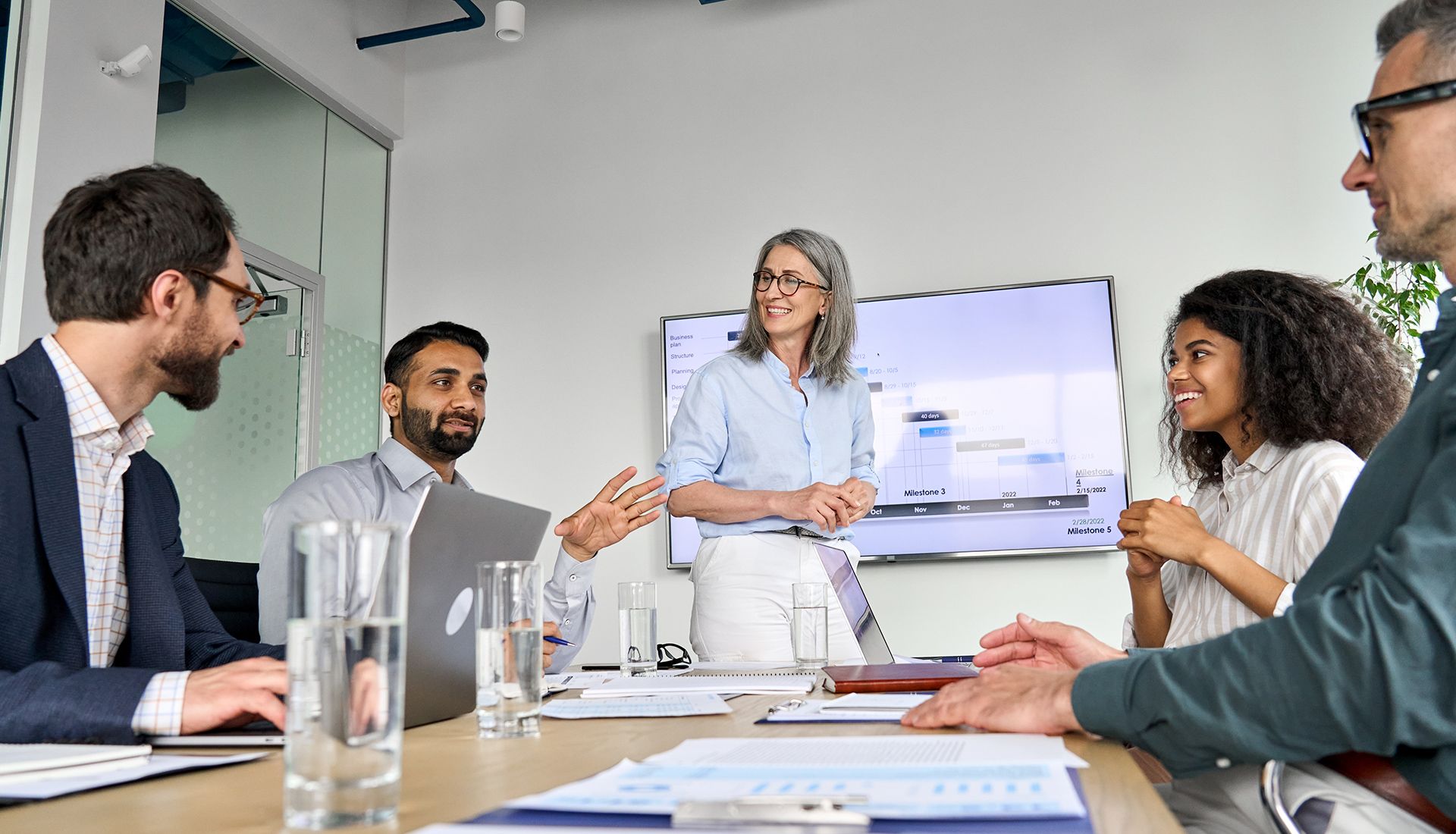 Business meeting with five colleagues around a conference table, discussing in a modern office.