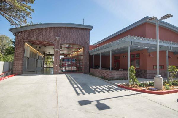 Modern brick building entrance with covered walkway, glass doors, and red trim in bright sunlight