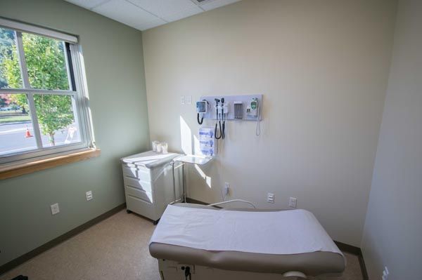Medical exam room with exam table, sink, and wall-mounted equipment by a window.